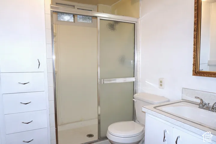 White vanity with integrated sink, chrome faucet, framed mirror, built-in storage cabinetry, and a shower with sliding glass doors
