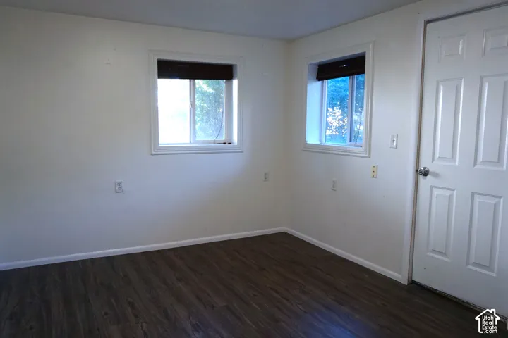 Dark wood-finish flooring with white baseboards, white walls, and two windows with blinds