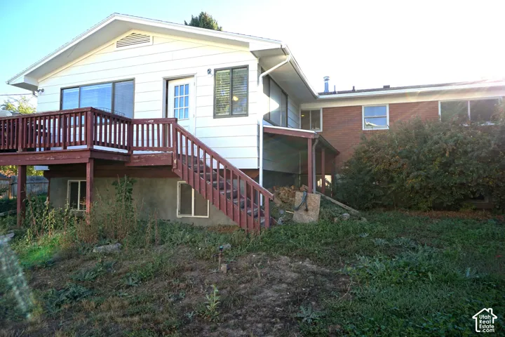 Exterior featuring white siding, a red-stained wood deck with stairs, a sliding glass door, and a brick facade section