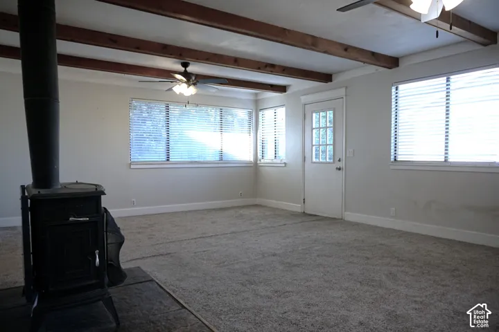 Exposed wood ceiling beams, wood-burning stove, multiple windows with blinds, ceiling fans, and a glass-paneled door