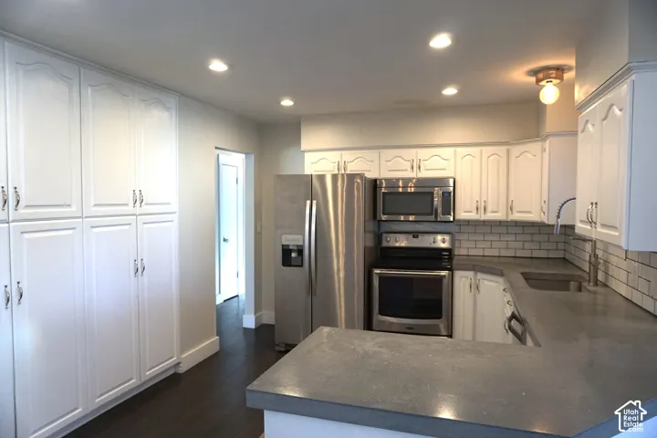White shaker-style cabinetry, stainless steel appliances, solid surface countertops, subway tile backsplash, and recessed lighting