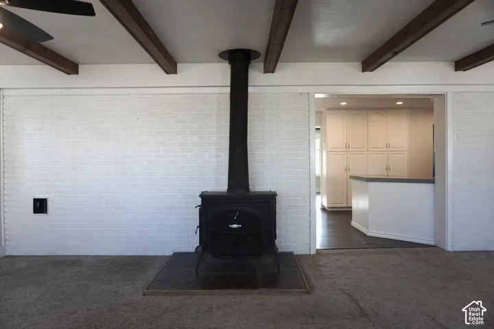 Exposed wood ceiling beams, white painted brick wall, black wood-burning stove, dark tile hearth, and white cabinetry
