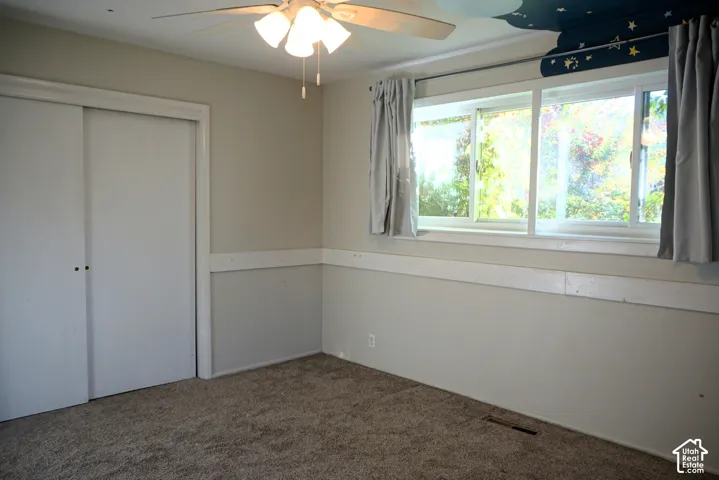 Room featuring a ceiling fan with integrated lighting, a multi-pane window, and carpeted flooring