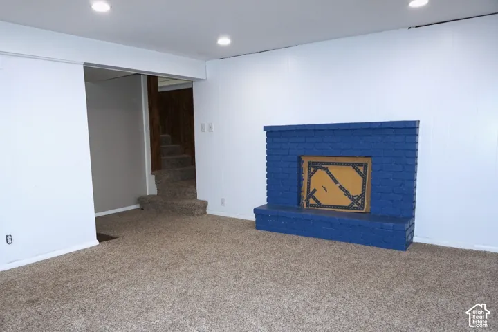 Carpeted flooring, white wall paneling, recessed lighting, and a painted brick fireplace