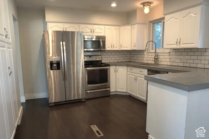 Kitchen featuring white shaker-style cabinetry, wood-finish flooring, subway tile backsplash, and stainless steel appliances