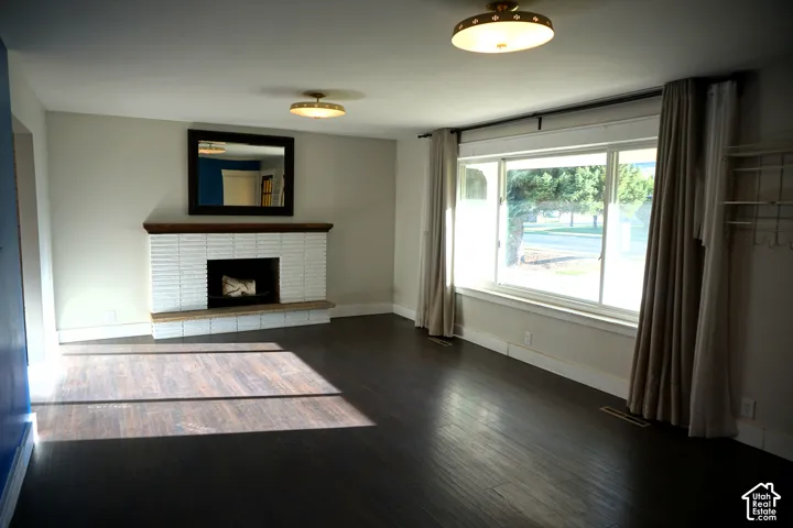 Wood-finish flooring, white brick fireplace with dark wood mantel, built-in shelving, and two ceiling-mounted light fixtures