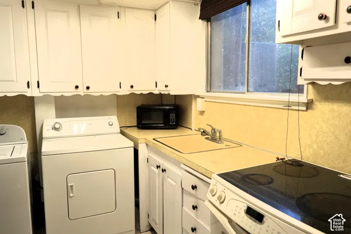 White cabinetry with black hardware, light-toned countertops, and a window with a blind