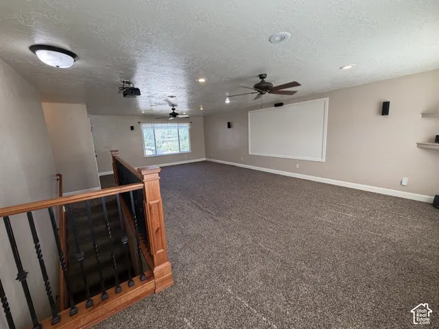 Spacious media room featuring a large projection screen, recessed lighting, ceiling fans, and built-in speakers
