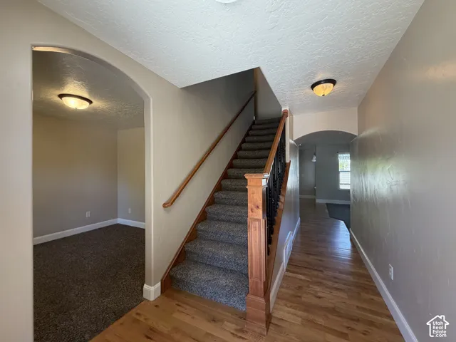 Hardwood flooring, carpeted staircase, wood banister with black spindles, arched doorways, and flush mount lighting