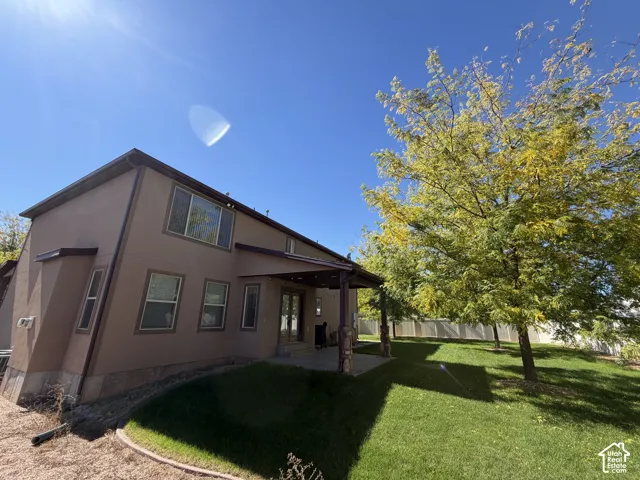 Stucco exterior with multiple windows, covered patio, mature trees, and a spacious lawn