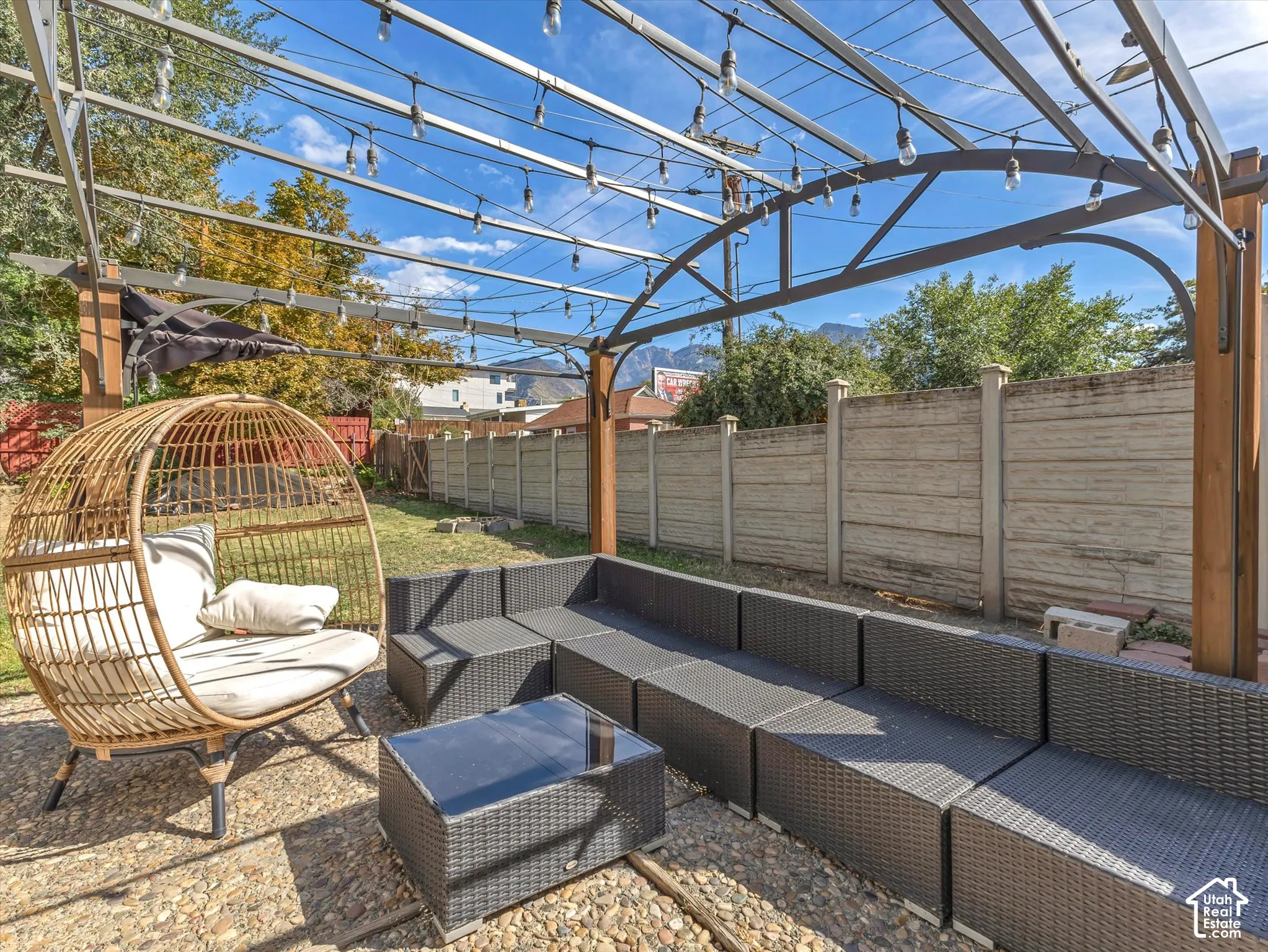 Outdoor living space featuring an open metal pergola, string lights, and a concrete perimeter fence