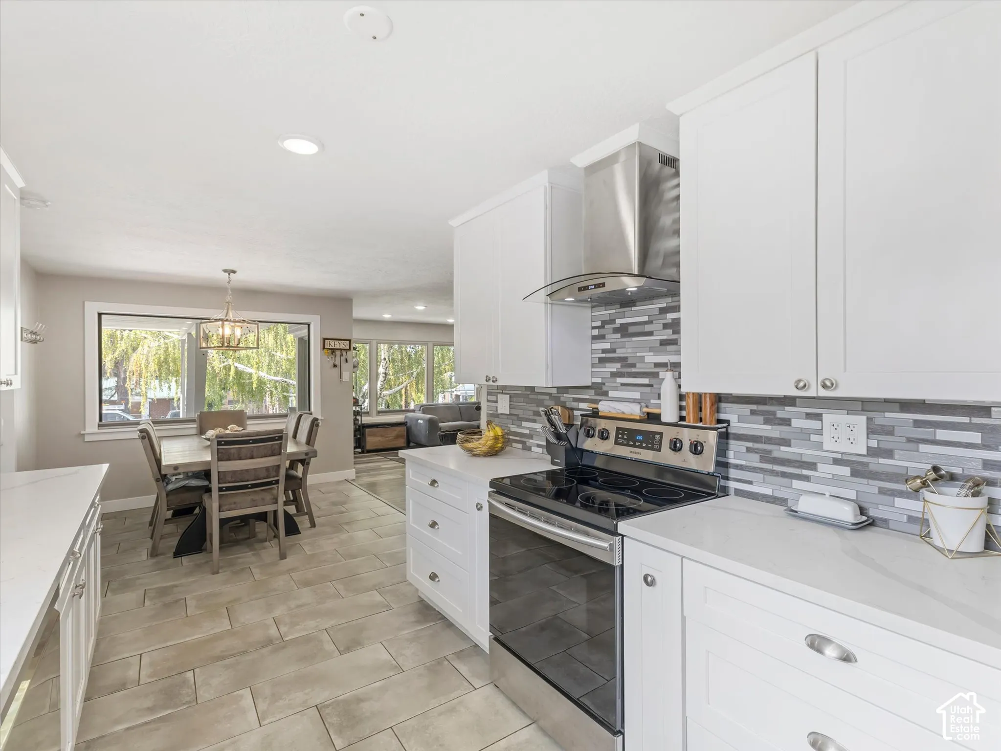White shaker-style cabinetry with chrome hardware, stainless steel appliances, patterned tile backsplash, light-toned plank-style flooring, and recessed ceiling lighting