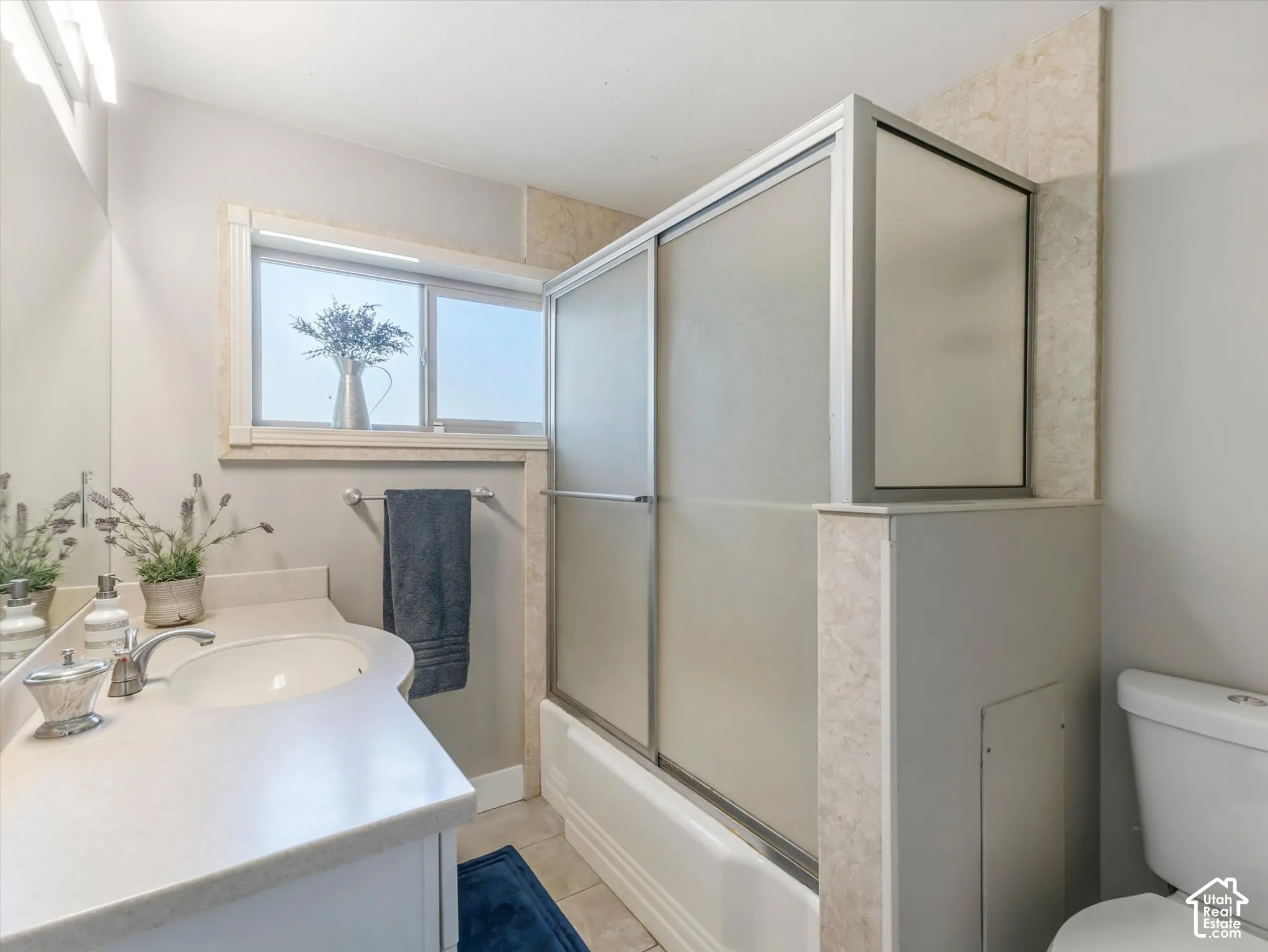 Single vanity with an integrated sink, shower-tub combination with sliding glass doors, and a window for natural light