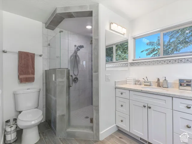 Glass-enclosed shower with tile surround, white vanity with stone countertop, wood-finish flooring, and horizontal windows