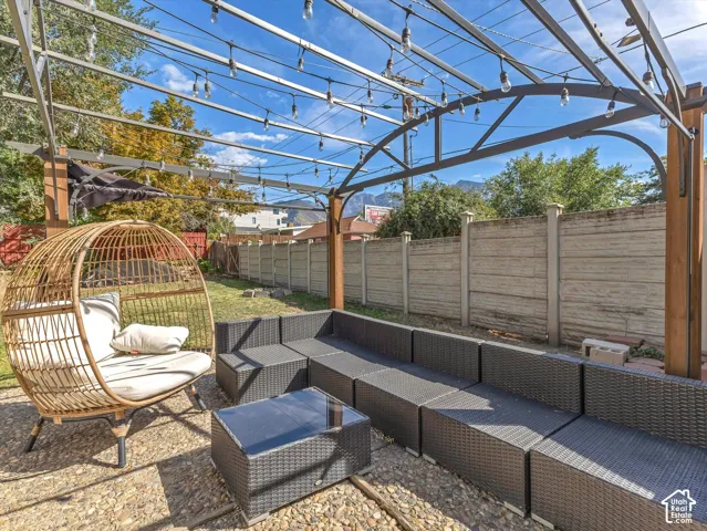 Outdoor living space featuring an open metal pergola, string lights, and a concrete perimeter fence