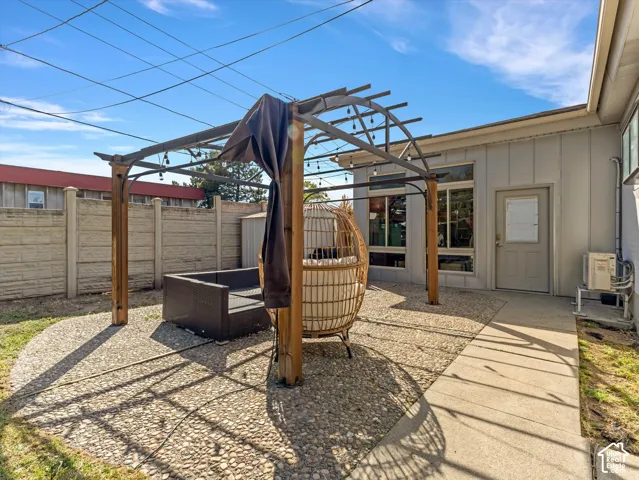 Gravel patio area with a wooden pergola, concrete pathway, and a privacy fence