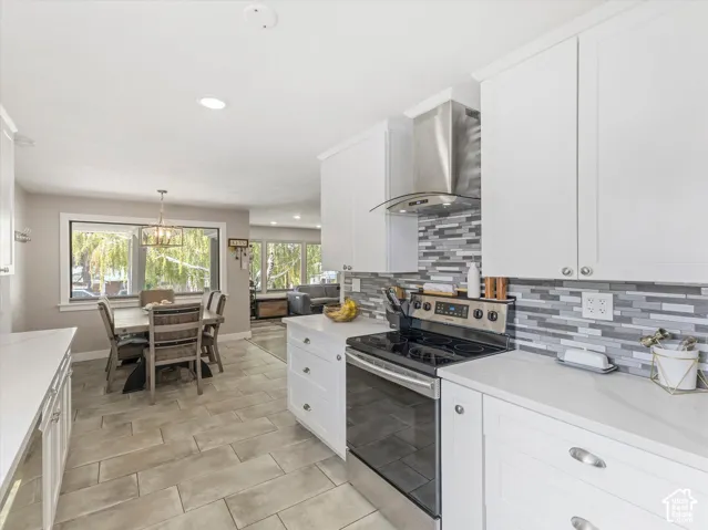 White shaker-style cabinetry with chrome hardware, stainless steel appliances, patterned tile backsplash, light-toned plank-style flooring, and recessed ceiling lighting