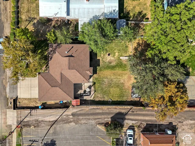 Pitched roofline, concrete driveway, fenced yard, mature trees, and paved street