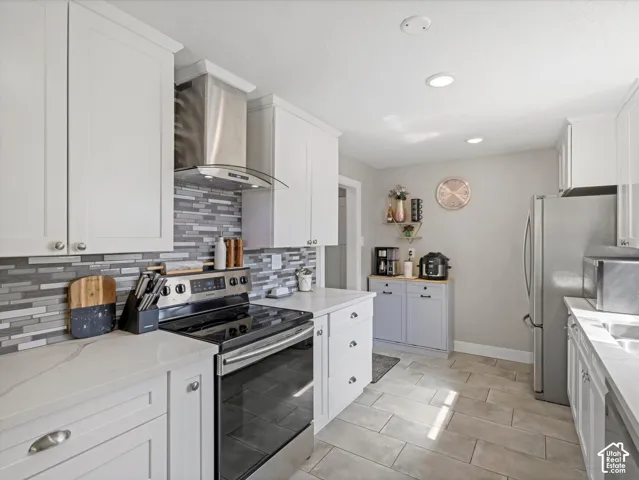 White shaker-style cabinetry with chrome hardware, an integrated stainless steel range hood, stone-look tile flooring, and quartz countertops with a mosaic tile backsplash