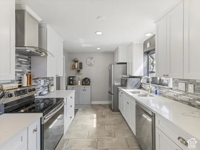 Kitchen featuring white shaker cabinetry, stainless steel appliances, light-toned countertops, tile flooring, and a mosaic tile backsplash