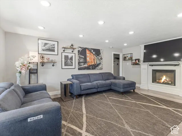 Recessed lighting, wood-finish flooring, and a fireplace with a white mantel and surround