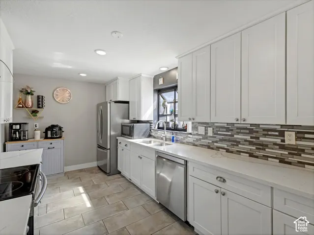 White shaker cabinetry, stainless steel appliances, tile flooring, mosaic tile backsplash, and light-toned countertops