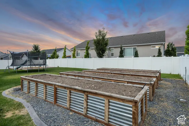 Backyard featuring multiple raised garden beds with corrugated metal and wood-finish construction, surrounded by a gravel bed and a white privacy fence