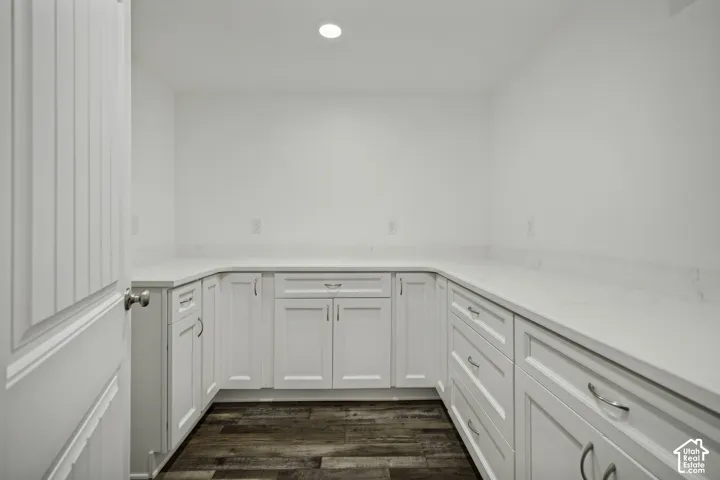 Wraparound white cabinetry, light-toned countertops, wood-finish flooring, and recessed ceiling lighting