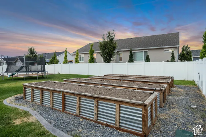 Backyard featuring multiple raised garden beds with corrugated metal siding, a white privacy fence, and a manicured lawn