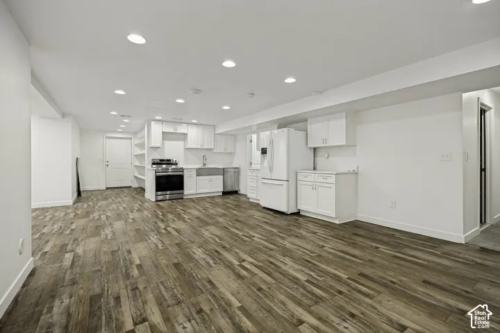 Open-concept lower level featuring wood-finish flooring, recessed lighting, a full kitchen with white cabinetry, stainless steel appliances, and a farmhouse sink