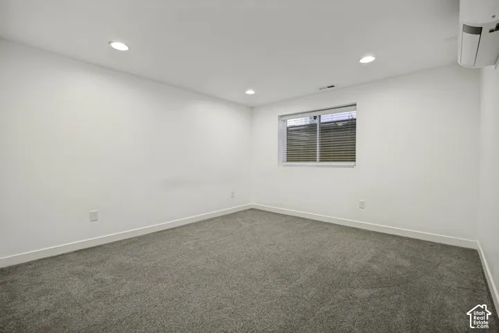 Gray carpeted flooring, white painted walls, recessed ceiling lighting, and a white window blind