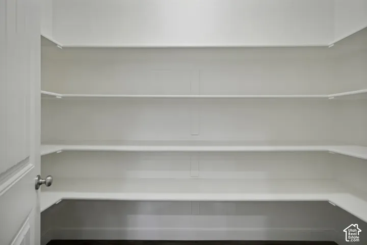Spacious pantry with multiple white shelves and dark flooring