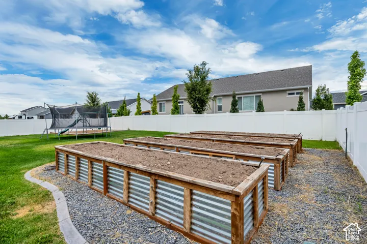 Expansive backyard featuring a manicured lawn, white privacy fencing, and multiple raised garden beds with wood and corrugated metal construction