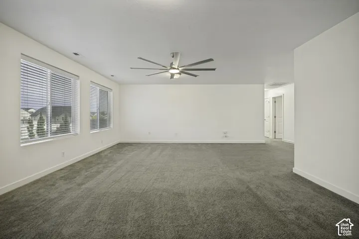 Spacious room featuring neutral carpeting, multiple windows with blinds, a modern ceiling fan, and recessed lighting