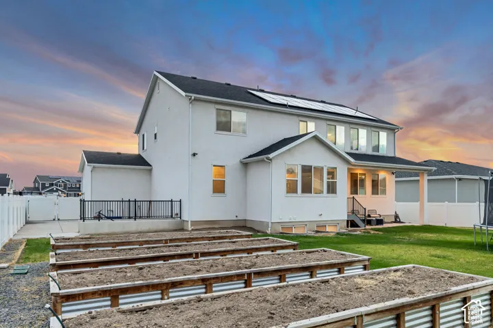 Rear exterior featuring multiple raised garden beds, a manicured lawn, a white vinyl fence, and a patio with steps