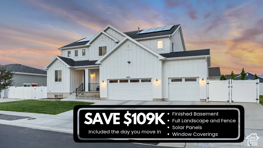 Multi-level exterior featuring white vertical siding, a three-car garage, roof-mounted solar panels, and perimeter privacy fencing