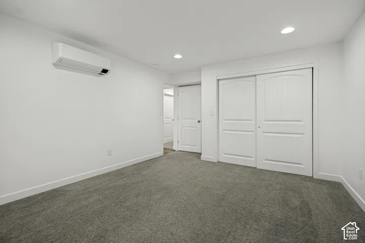 Wall-mounted HVAC unit, recessed lighting, gray carpet flooring, white sliding closet doors, and white paneled interior doors