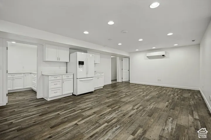 Wood-finish flooring, recessed lighting, white cabinetry, white refrigerator, and a wall-mounted climate control unit
