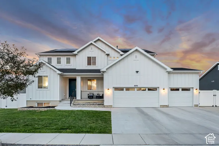 White board and batten exterior with dark trim windows, covered front porch, dual garage doors, and front yard landscaping
