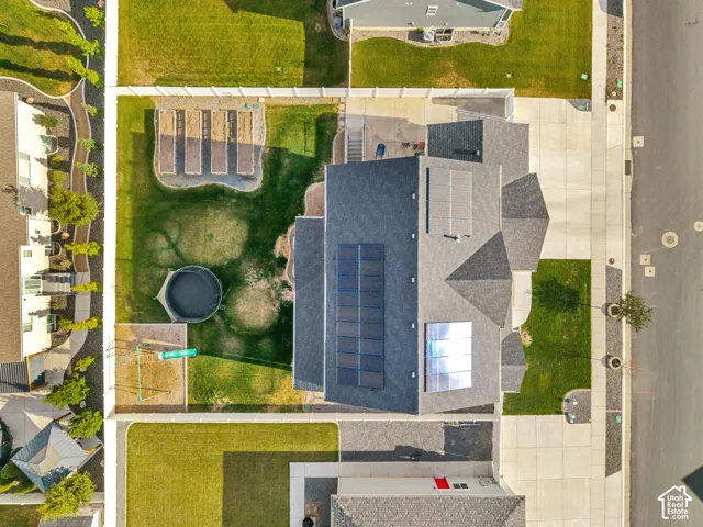 Expansive residential property featuring a shingle roof, solar panels, a concrete driveway, a grass lawn, and raised garden beds