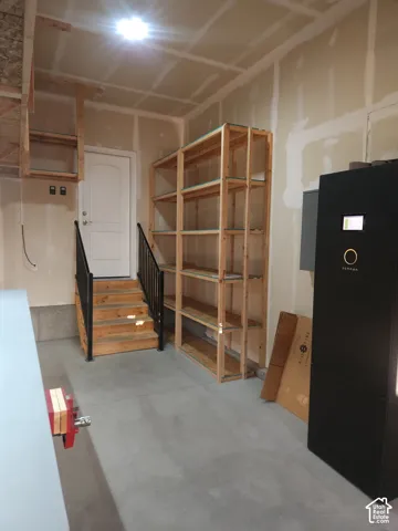 Concrete flooring, built-in wooden shelving, wooden staircase with black metal handrails, white door, overhead lighting