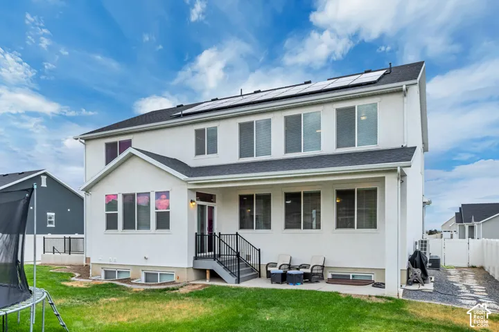 White stucco exterior with a multi-level roofline, solar panels, a walk-out patio, and an exterior staircase with metal railings