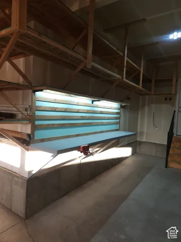Built-in workbench with integrated lighting, overhead wooden shelving, concrete flooring, and concrete wall foundation