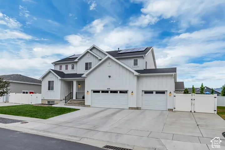 Modern farmhouse exterior with white vertical siding, dual garage doors, a concrete driveway, and solar panels