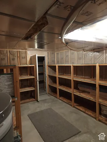 Concrete flooring, built-in wooden shelving, and an unfinished ceiling with exposed insulation