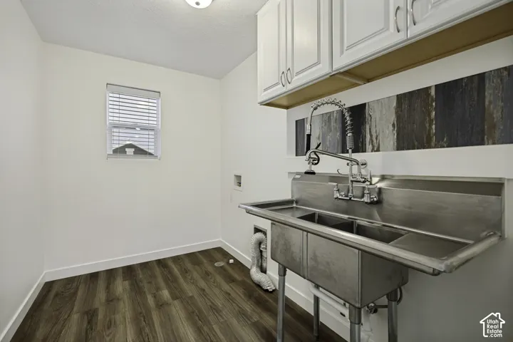 White shaker-style cabinetry with chrome hardware, a wall-mounted utility sink with a dual-faucet system, and wood-finish flooring