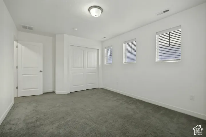 Recessed ceiling light fixture, three windows with blinds, gray carpet, and white paneled doors
