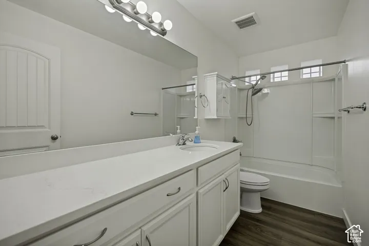 White vanity with integrated sink, white countertop, dark wood-finish flooring, and a white shower/tub combination with a showerhead