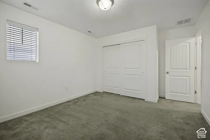 Neutral-toned carpeting, white walls, and a window with horizontal blinds provide natural light