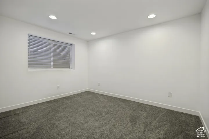 Recessed ceiling lighting, white walls, gray textured carpeting, and a window with horizontal blinds
